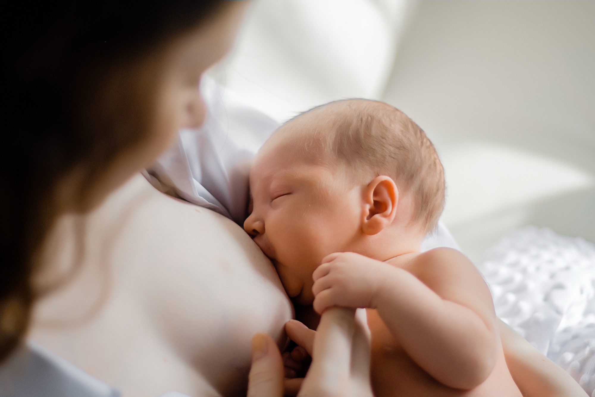 A mother breastfeeding her newborn in soft window light